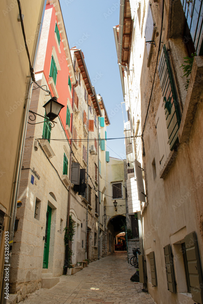 Obraz premium Tiny beige street on the summer day, narrow cobblestone alleyway between tall buildings, mediterranean cityscape, Croatia, Rovinj.