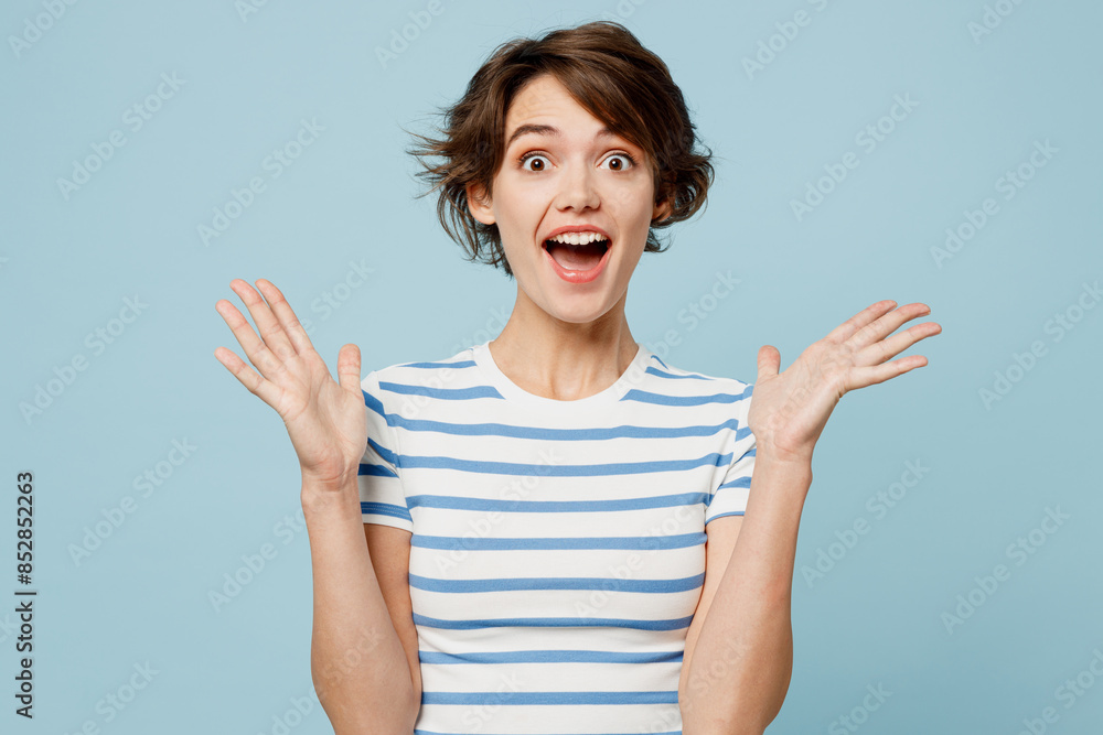 Fototapeta premium Young surprised shocked excited fun woman she wear striped t-shirt casual clothes look camera spread hands isolated on plain pastel light blue cyan color background studio portrait. Lifestyle concept.