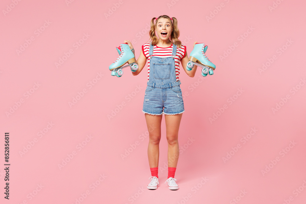Full body young shocked surprised woman wear red t-shirt denim overalls casual clothes hold in hand blue rollers look camera isolated on plain pink background. Summer sport lifestyle leisure concept. Full body young shocked surprised woman wear red t-shirt denim overalls casual clothes hold in hand blue rollers look camera isolated on plain pink background. Summer sport lifestyle leisure concept.