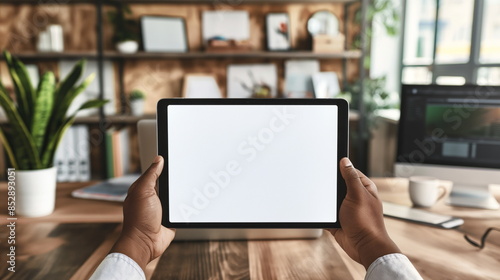 Close-up of hand with tablet mockup white screen, with out of focus modern office setting background