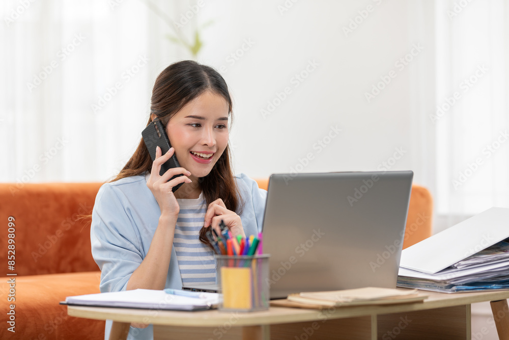 Asian Woman Engaged in Phone Call While Working on Laptop at Home Asian Woman Engaged in Phone Call While Working on Laptop at Home