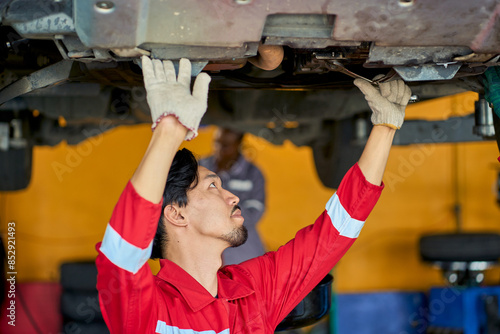 Asian technician male repir under the car or suspension in car garage. photo