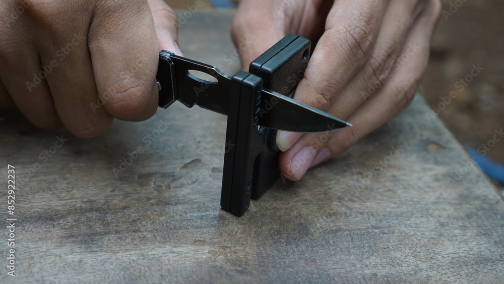 Fototapeta premium Man is sharpening a survival knife using a knife sharpener outdoors