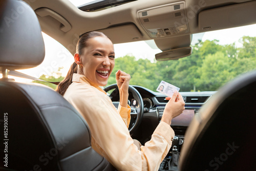 Foto Overjoyed European lady sitting in her own car and holding new driver license, c