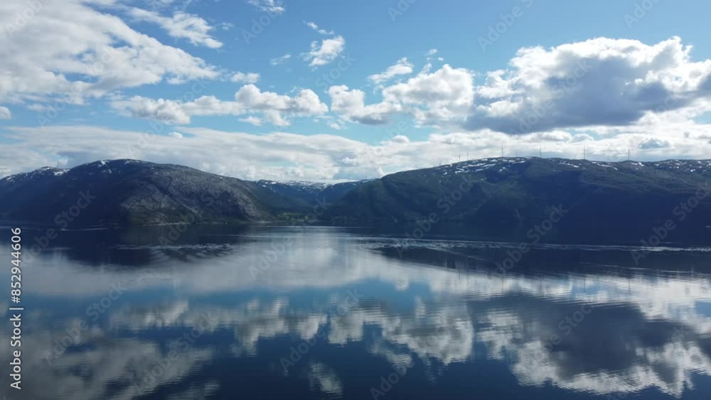calm fjord surface with sunshine and white cloud reflection with mighty mountain backdrop with windmill farm on top in northern norway, aerial video panning right calm fjord surface with sunshine and white cloud reflection with mighty mountain backdrop with windmill farm on top in northern norway, aerial video panning right