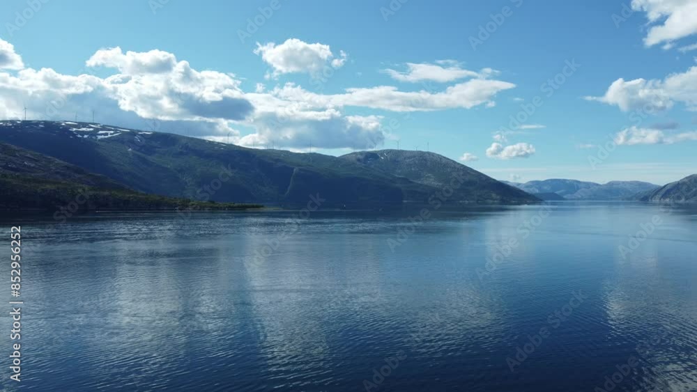 flying over calm blue fjord with mighty mountain in the background with windmill farm on top and pleasure boat moving over the water, aerial video flying over calm blue fjord with mighty mountain in the background with windmill farm on top and pleasure boat moving over the water, aerial video