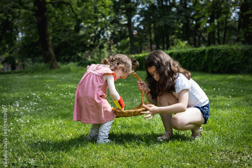 Fototapeta premium Portrait of two girls decorate a basket with daisies on a summer day.