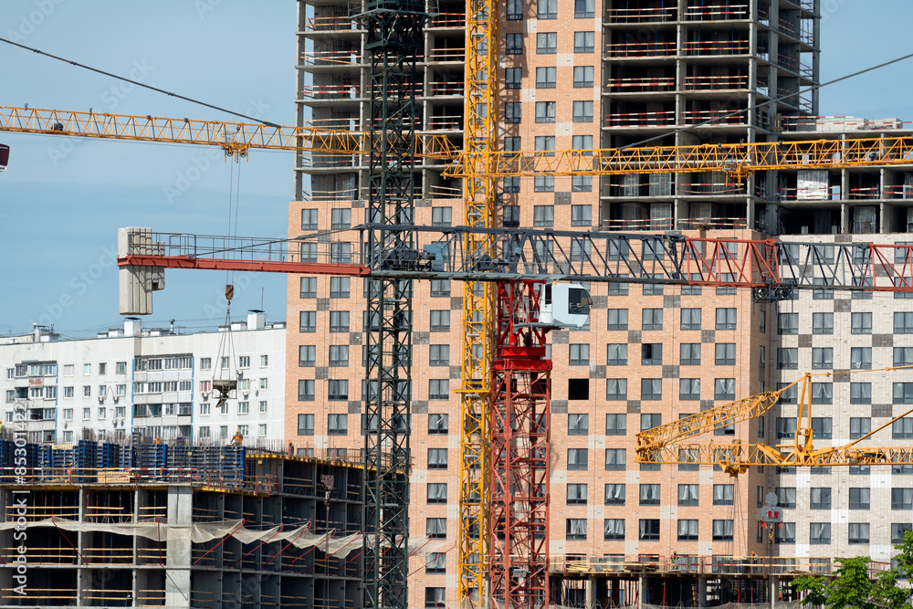 Tower cranes in close-up against the background of a multi-storey building under construction Tower cranes in close-up against the background of a multi-storey building under construction