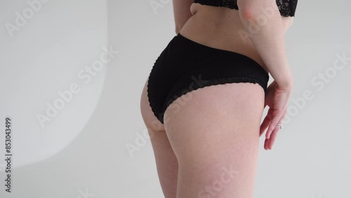 Close-up view of sexy slim caucasian woman standing against grey background. Woman wears black lace panties. Soft focus. Real time video. Fashion and sensuality theme.