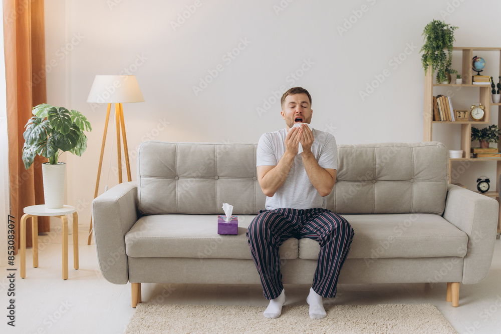 Bearded sick sad man sits on couch at home suffers from runny nose flu disease coronavirus pandemic covid epidemic sneezes. Bearded sick sad man sits on couch at home suffers from runny nose flu disease coronavirus pandemic covid epidemic sneezes.