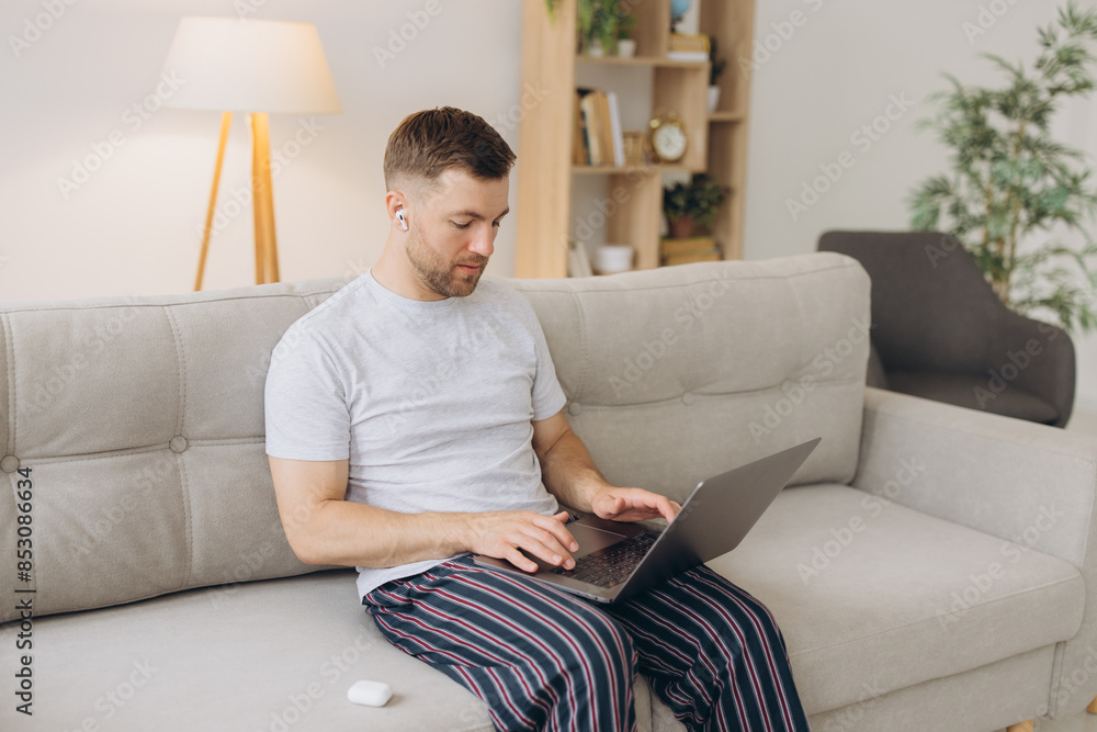One man caucasian male freelancer work from home with headphones on his head on laptop computer customer support dispatcher while sit on sofa bed at home in shirt and pajamas happy smile One man caucasian male freelancer work from home with headphones on his head on laptop computer customer support dispatcher while sit on sofa bed at home in shirt and pajamas happy smile