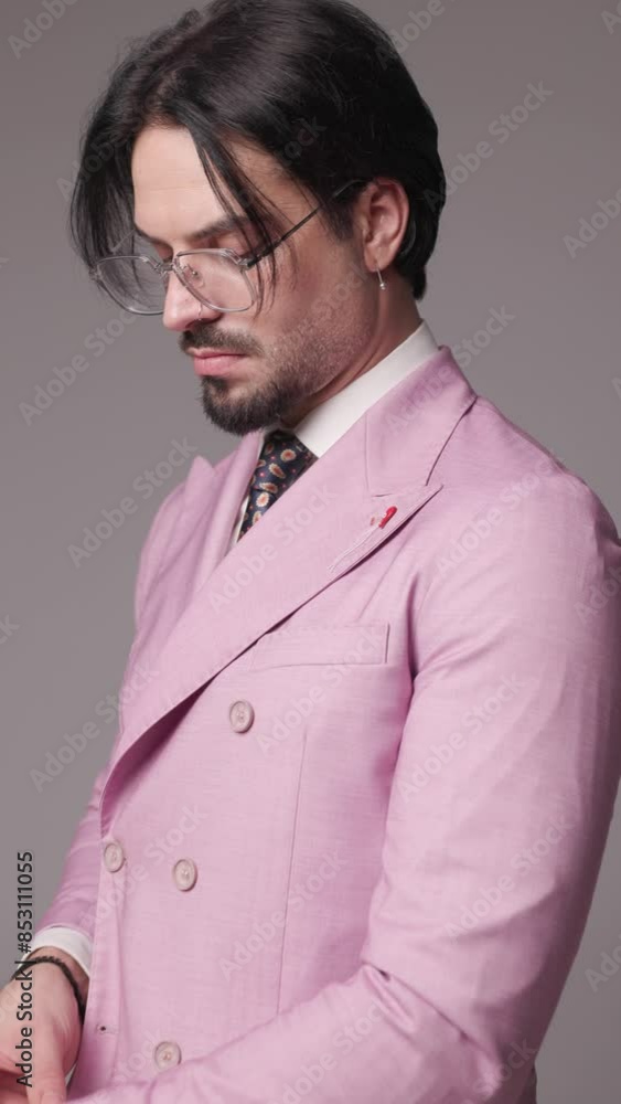 project video of elegant businessman with glasses in double breasted pink suit adjusting sleeves and tie and looking to side when camera is closing up on grey background project video of elegant businessman with glasses in double breasted pink suit adjusting sleeves and tie and looking to side when camera is closing up on grey background
