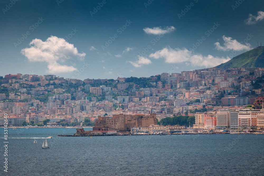 Fototapeta premium The photo captures Naples' vibrant harbor in golden light, A mix of fishing boats and yachts dot the clear blue waters, reflecting the lively maritime activity. 