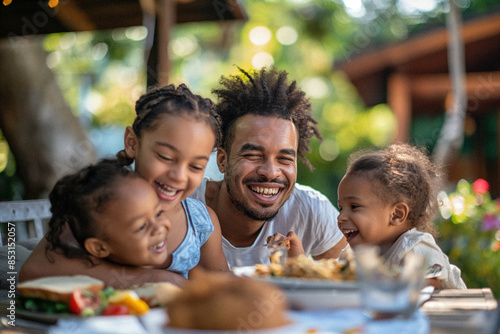 A diverse young family enjoying a summer day being outside together eating lunch in their beautiful backyard laughing with each other. Themes of unity, happiness and family
