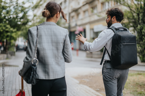 Two business professionals walking and discussing work outdoors on a city street. They appear to be engaged in a serious conversation. © qunica.com