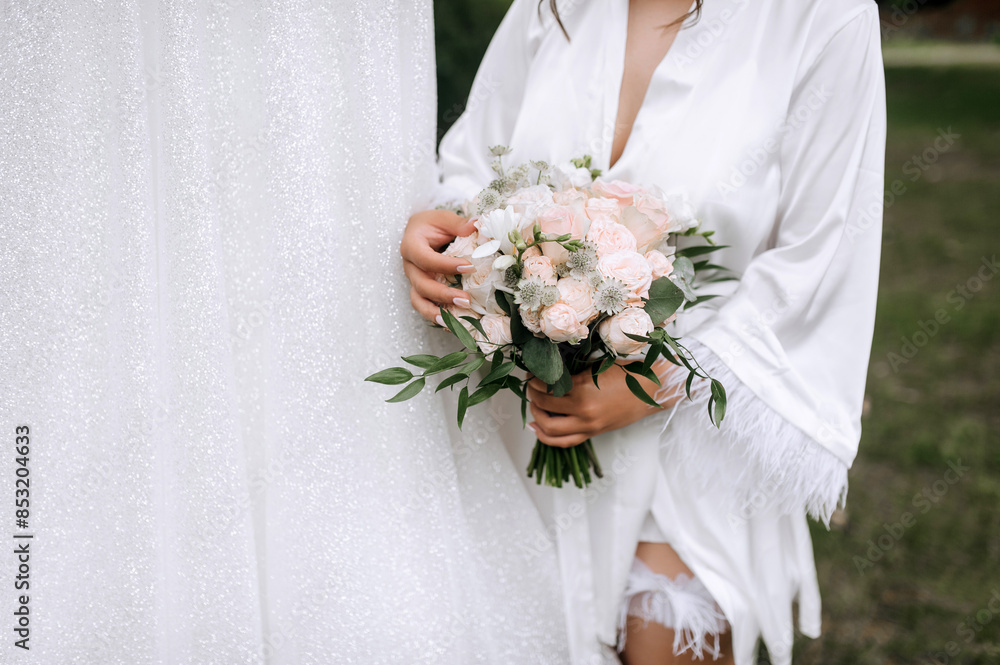 A bride in a white dress holds in her hands a beautiful bouquet of roses and wildflowers outdoors. Wedding photography, lifestyle. A bride in a white dress holds in her hands a beautiful bouquet of roses and wildflowers outdoors. Wedding photography, lifestyle.