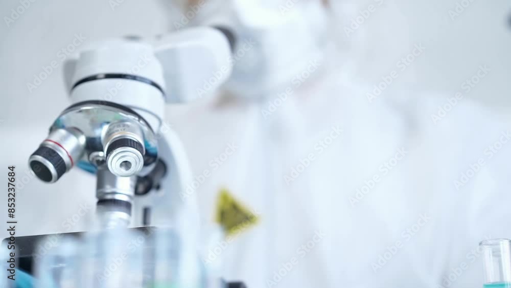 Professional scientist in protective gear is using microscope in a laboratory setting, close-up. Science and medicine concepts Professional scientist in protective gear is using microscope in a laboratory setting, close-up. Science and medicine concepts