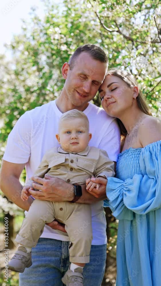 Happy Caucasian couple with their adorable little baby. Loving family of three in the garden in spring. Vertical video. Happy Caucasian couple with their adorable little baby. Loving family of three in the garden in spring. Vertical video.