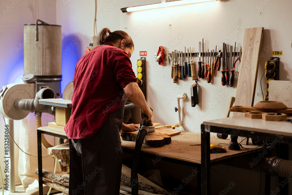 Artisan in studio using orbital sander with fine sandpaper on lumber to achieve smooth finish. Creative woodworker in carpentry shop uses angle grinder to create wood art Artisan in studio using orbital sander with fine sandpaper on lumber to achieve smooth finish. Creative woodworker in carpentry shop uses angle grinder to create wood art