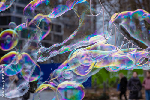 Many multicolored giant soap bubbles flying in the air on a windy day. Huge bubble are stretching on the wind into long smoothy changing form without popping. Close up. Copy space. Selective focus.
