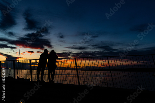 sagome nere di una coppia di persone irriconoscibili appoggiate ad una ringhiera mentre guardano tranquillamente un bellissimo tramonto sul mare Adriatico photo