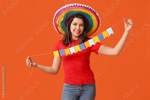 Beautiful young happy woman in sombrero with garland on orange background. Cinco de Mayo celebration