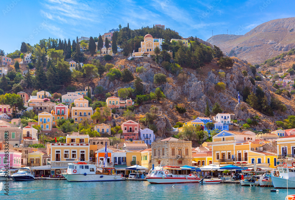 Naklejka premium Hillside view of the colorful buildings and busy harbor on Symi Island, Greece.
