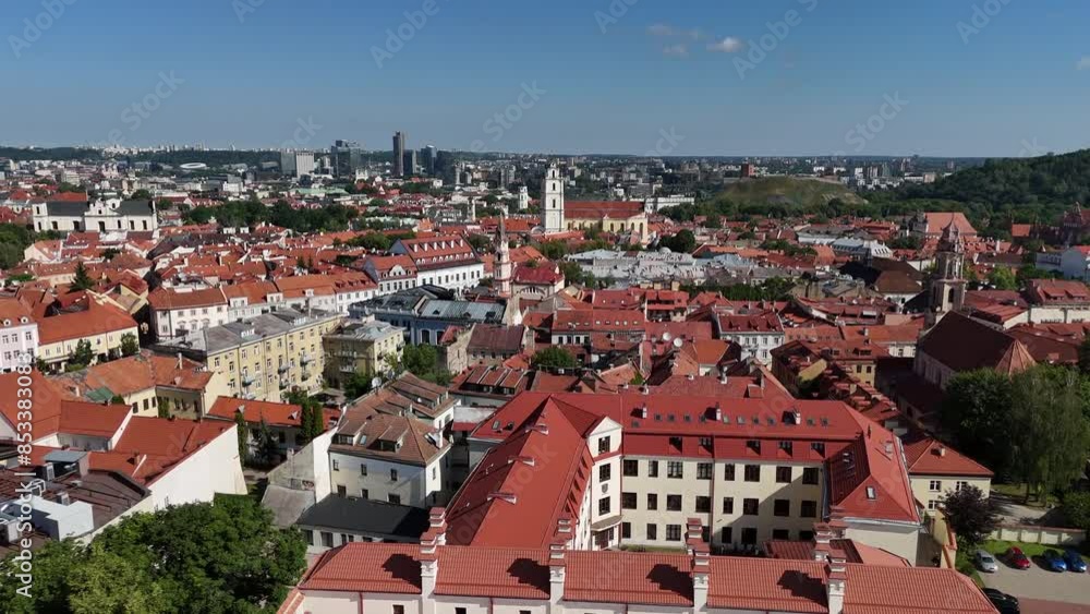 Aerial view of Vilnius old town featuring red rooftops, Gediminas Tower on a hill, and modern skyline buildings under a clear blue sky.