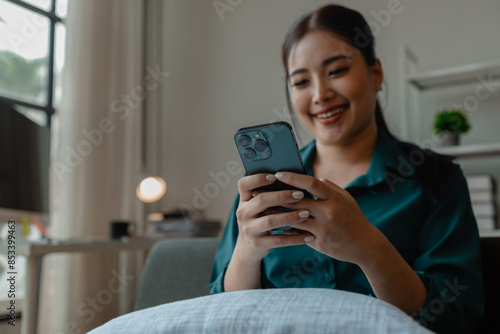a beautiful Asian woman is using her free time in workplace, an female employee is smiling and has a conversation with friend in the office, she feel enjoy on her smartphone