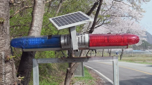 A flashing red and blue traffic light mounted on a aluminum frame, powered by a solar panel in rural South Korea