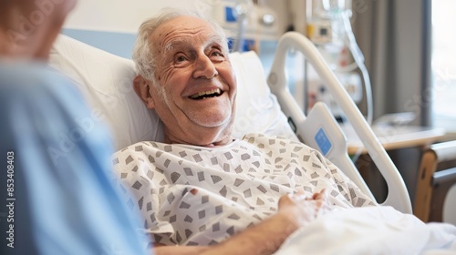 Senior patient laughing with visitor in hospital - Elderly man in a hospital gown laughs with a visitor, creating a light-hearted atmosphere