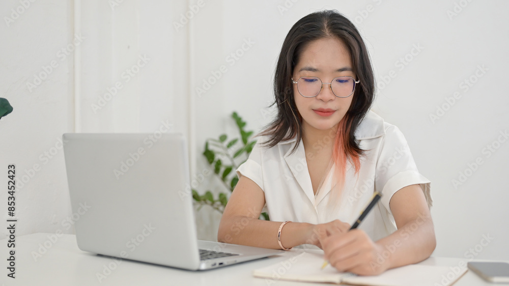 A focused young Asian female student doing homework or studying online in a coffee shop. A focused young Asian female student doing homework or studying online in a coffee shop.