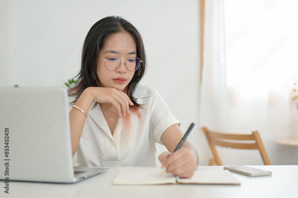 A focused young Asian female student doing homework or studying online in a coffee shop. A focused young Asian female student doing homework or studying online in a coffee shop.