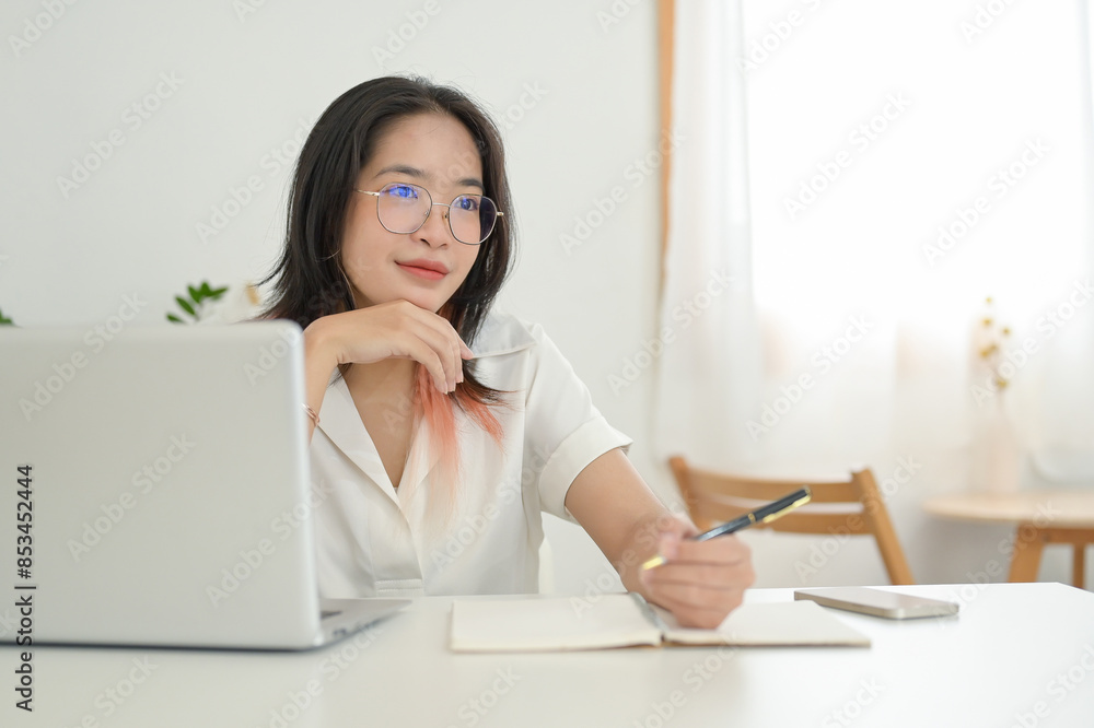 A positive Asian woman is daydreaming or pondering something while working remotely at a coffee shop A positive Asian woman is daydreaming or pondering something while working remotely at a coffee shop