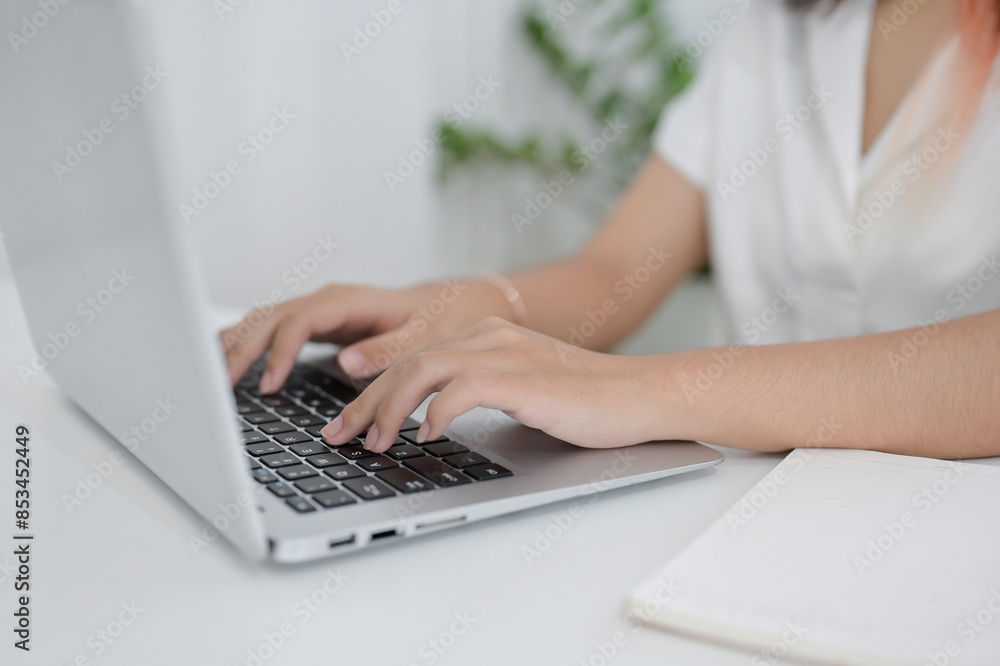 A cropped image of an Asian woman working on her computer at a table indoors, typing on the keyboard A cropped image of an Asian woman working on her computer at a table indoors, typing on the keyboard
