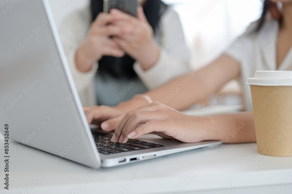 A cropped image of a female working on her laptop while sitting with her friend in a coffee shop. A cropped image of a female working on her laptop while sitting with her friend in a coffee shop.