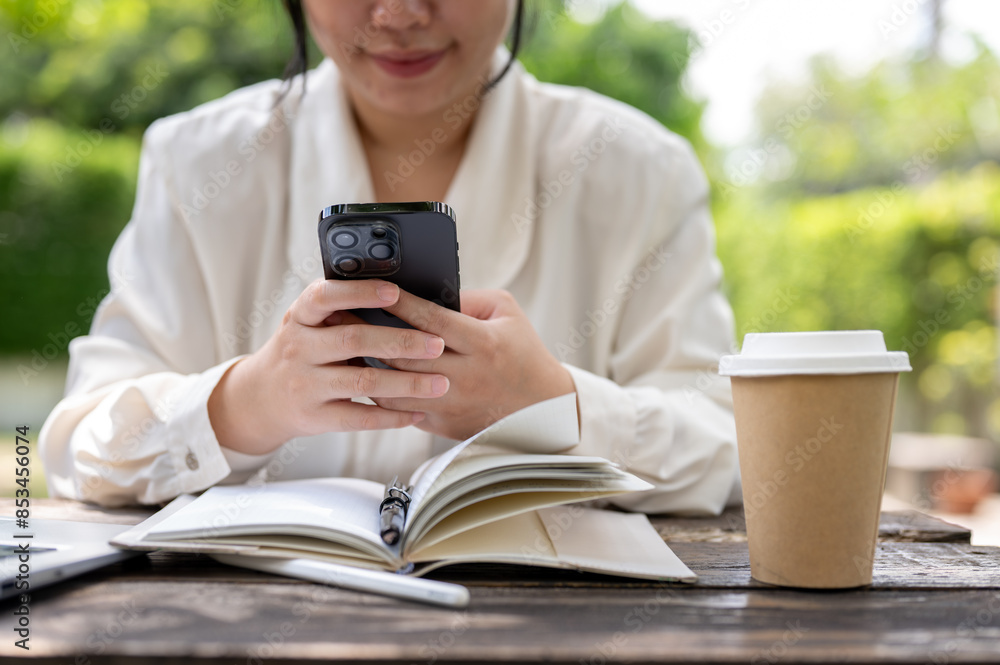 A cropped image of a woman using her smartphone while working at a table in a garden. A cropped image of a woman using her smartphone while working at a table in a garden.