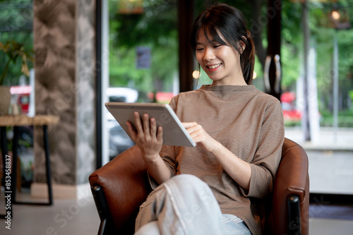 Free Download A pretty, positive young Asian woman using her digital tablet in a coffee shop. - GFXLoad