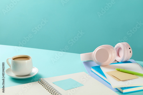 Creative flat lay photo of workspace desk with paper document, notebooks, a pink headphone and a cup of hot coffee, against on blue color background. Advertising and copy space, high angle view photo