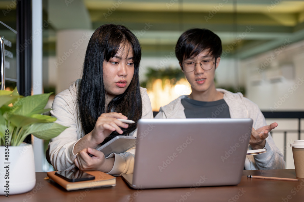 Two young Asian college student friends are working on a co-project together at a cafe. Two young Asian college student friends are working on a co-project together at a cafe.