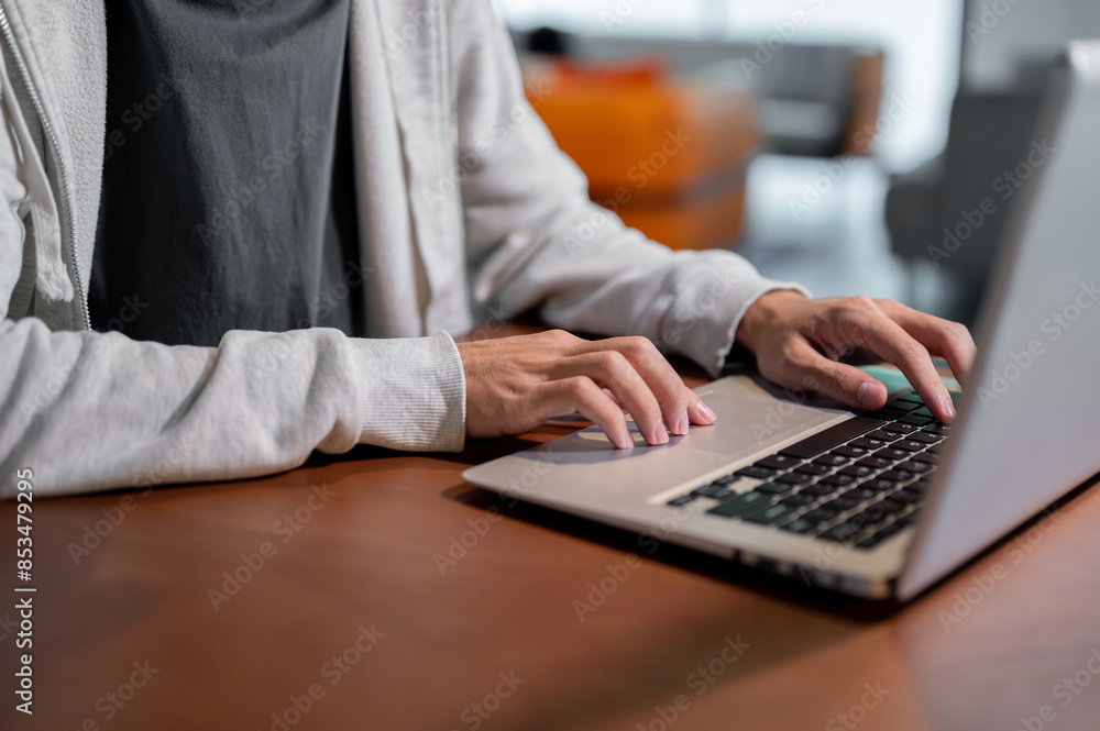 A close-up image of an Asian man in comfy clothes working on his laptop computer, working indoors. A close-up image of an Asian man in comfy clothes working on his laptop computer, working indoors.