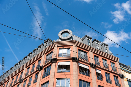 A tall building with a clock on top. The clock is surrounded by wires. The building is red and has a lot of windows