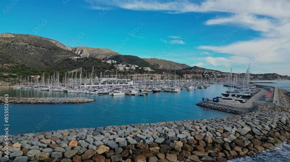 Sailboats docked at Port of Ginesta with mountains in the background under a bright blue sky Sailboats docked at Port of Ginesta with mountains in the background under a bright blue sky