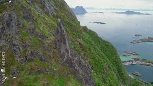 Aerial view in orbit over the rocky pinnacle of Svolvaergeita (The Goat) and where a climber can be seen in the distance. In Lofoten, Norway. photo