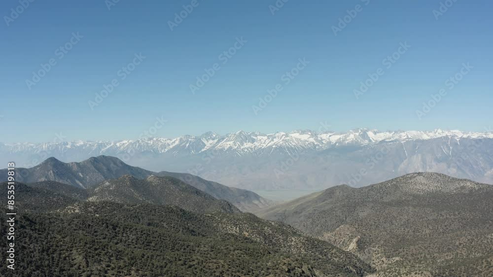 A beautiful pan shot from left to right captures green hills with majestic mountains in the background, their tops covered in glacier snow, all under a clear blue sky. A beautiful pan shot from left to right captures green hills with majestic mountains in the background, their tops covered in glacier snow, all under a clear blue sky.