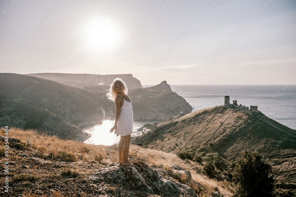 Naklejka premium A woman stands on a hill overlooking a body of water. The sky is clear and the sun is shining brightly. The woman is enjoying the view and the peaceful atmosphere.