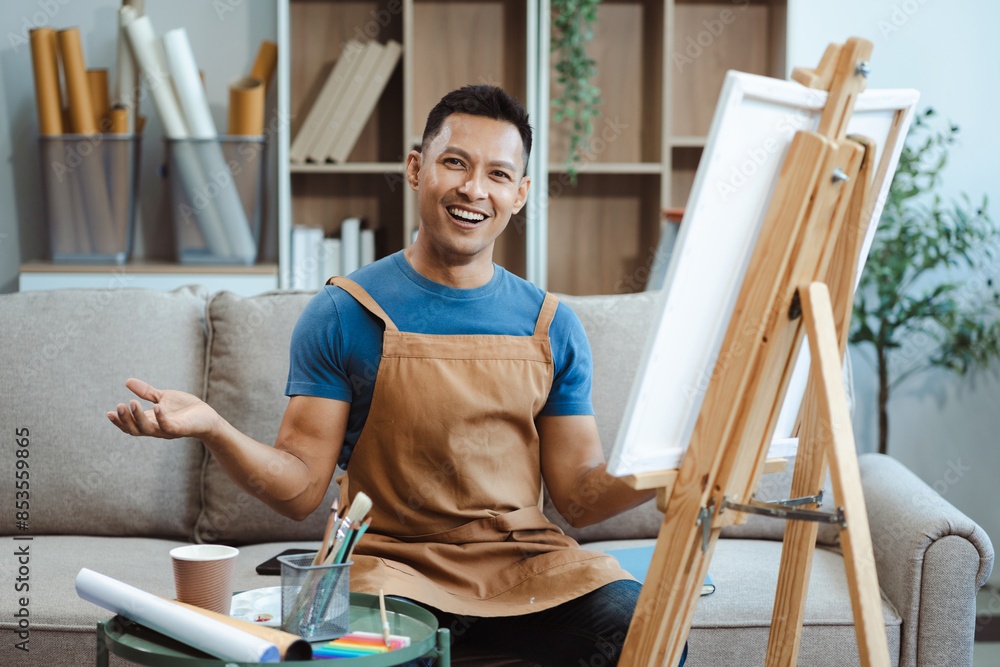 Creative painter painting in an art studio. Artistic young man working on a new painting. Cheerful young artist looking at the camera while holding a paintbrush. Creative painter painting in an art studio. Artistic young man working on a new painting. Cheerful young artist looking at the camera while holding a paintbrush.