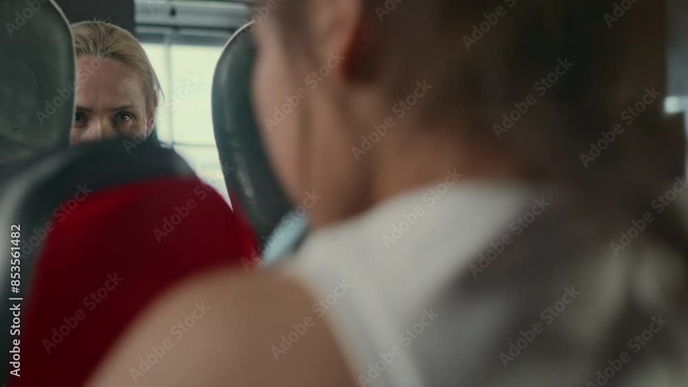 Medium close-up of calm, focused 50-year-old Caucasian female boxing instructor holding up punch mitts while working with young competitive boxer, preparing for championship Medium close-up of calm, focused 50-year-old Caucasian female boxing instructor holding up punch mitts while working with young competitive boxer, preparing for championship