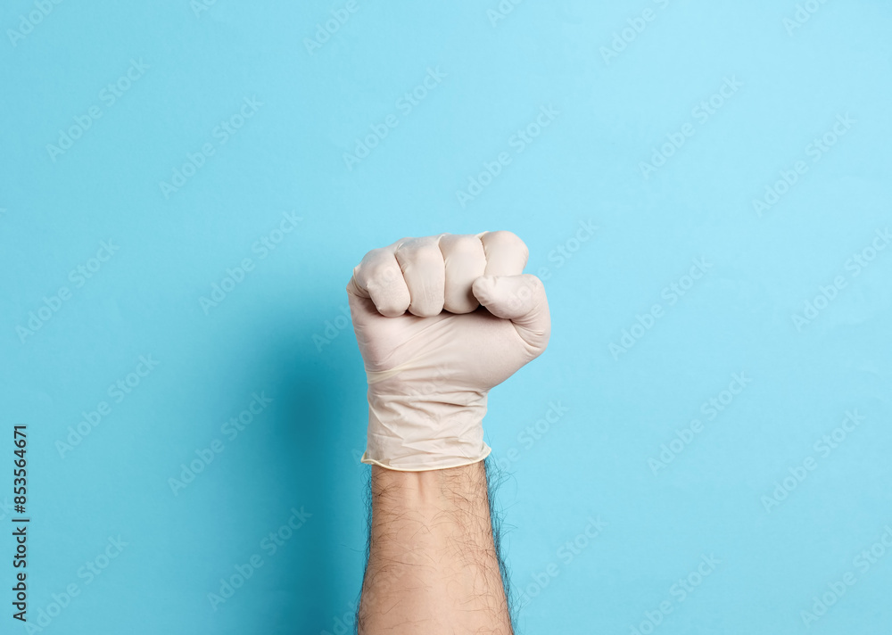 Male hand wearing a white latex medical glove making a fist, on a blue background Male hand wearing a white latex medical glove making a fist, on a blue background