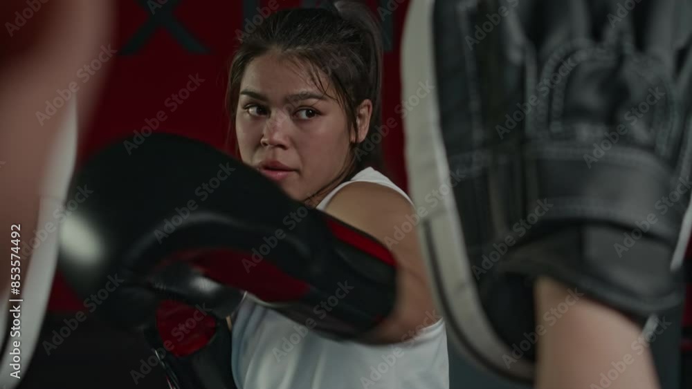 Medium close-up over-shoulder shot of 20-year-old Hispanic professional combat or MMA fighter having vigorous boxing workout, performing alternating jabs at punch mitts held by unrecognizable coach Medium close-up over-shoulder shot of 20-year-old Hispanic professional combat or MMA fighter having vigorous boxing workout, performing alternating jabs at punch mitts held by unrecognizable coach
